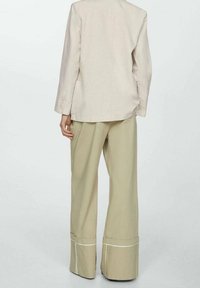 Béžové na míru ušité sako a široké kalhoty, texturovaná látka, bílé lemování na kalhotách, minimalistický design, funkční zadní kapsy na saku.