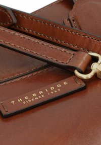 Borsa in pelle marrone con hardware dorato, una tracolla staccabile e un'etichetta con la scritta "THE BRIDGE" e "FIRENZE 1969".