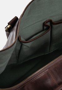 Innenraum einer braunen Ledertasche mit grünem Stofffutter, ausgestattet mit zwei Seitentaschen und einem Reißverschluss entlang der oberen Kante.