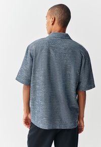 Kort mouwen overhemd met knopen in blauwe en witte gestructureerde stof met een traditionele kraag en rechte zoom, van achteren weergegeven.