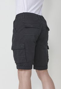 Shorts cargo noirs en mélange de coton, dotés de plusieurs poches latérales et d'un ourlet roulé, avec une taille élastique pour plus de confort.