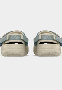 Paire de sandales beige avec des semelles texturées et des brides en tissu bleu réglables, vues de dos sur un fond blanc uni.