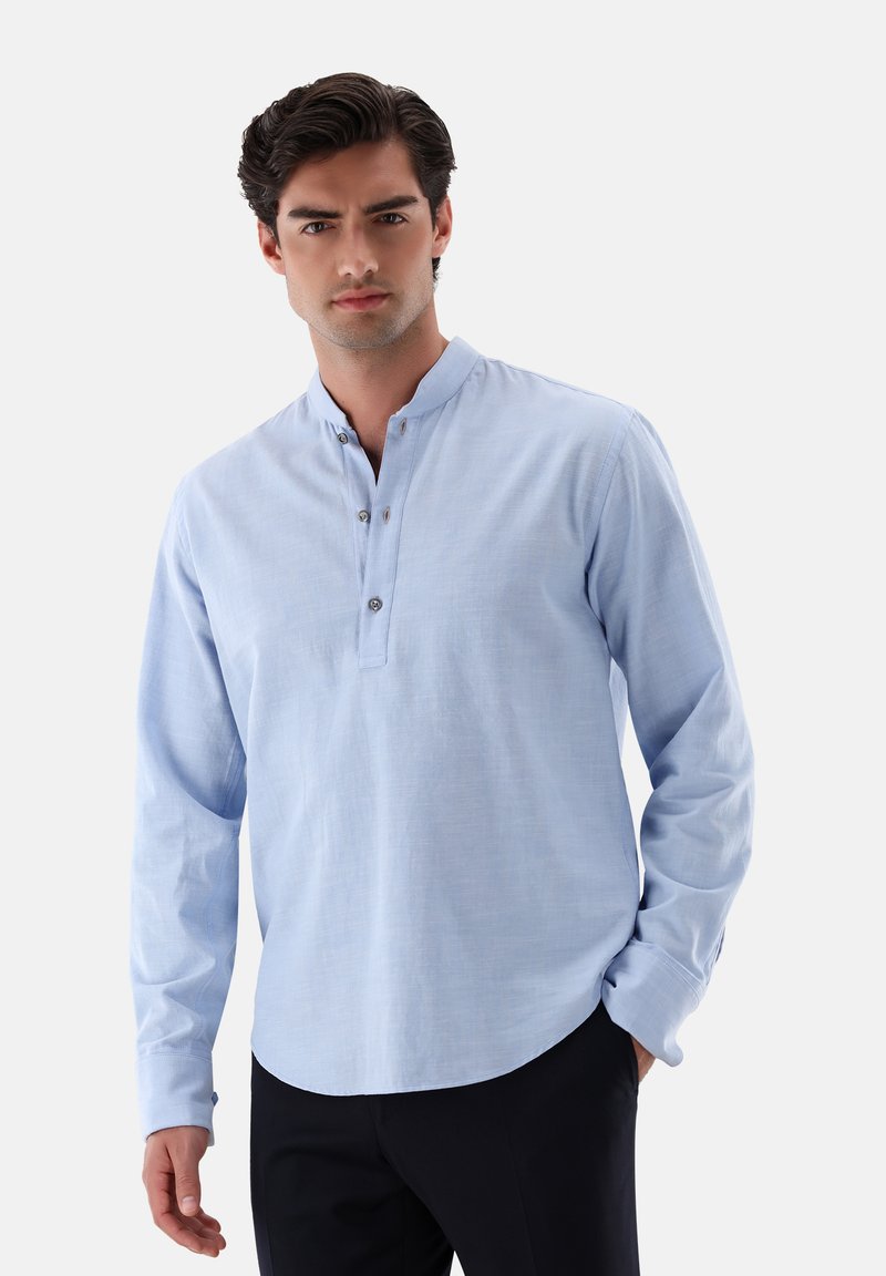 Camicia azzurro chiaro a maniche lunghe con colletto alla coreana, chiusura con bottoni e un tessuto morbido e con texture. Vestibilità su misura con orlo leggermente arrotondato.