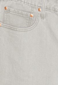 Ljust grå denimtyg med en framficka försedd med kopparnitar. Slät textur och avslappnad design med subtila sömmar.