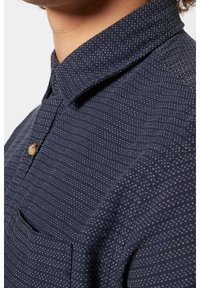 Mörkblå skjorta i strukturerad tyg, med ett subtilt mönster av små, ljusa prickar och en knapp-upplagd krage.