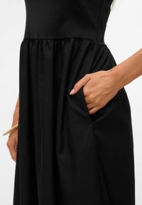 Vestido negro con un corsé ajustado y falda acampanada, con un bolsillo visible en el lateral y una textura de tela suave.