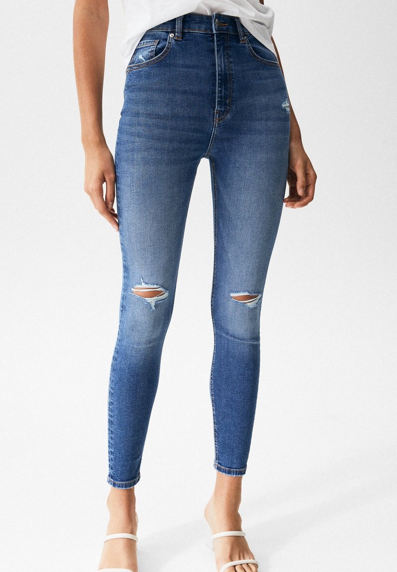 High-waisted, skinny jeans in medium blue denim with distressed knee rips. Features a classic five-pocket design and slight fading.