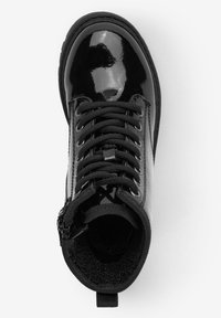 Bottine en cuir verni noir avec lacets noirs, bout rond, col rembourré et fermeture éclair latérale. Doublure intérieure texturée pour plus de confort.