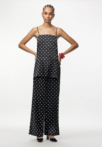 Melnas un baltas punktuota bezraku blūze un platām biksēm, ar gludu satīna tekstūru, slāņotu dizainu un plānām siksnām.