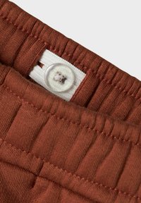 Rustfarvet taljeelastik med elastisk struktur, udstyret med en knap og et hvidt label til størrelse. Synlige stiklinjer forstærker strukturen.