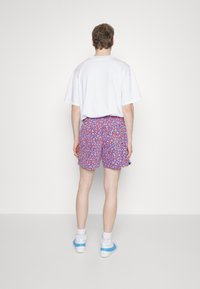 Kortärmad vit t-shirt tillsammans med färgglada shorts med blommönster i lila, röd och rosa, designade med ett elastiskt midjeband.
