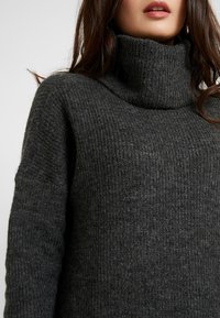 Maglione a coste grigio scuro con un design a collo alto e superficie testurizzata, dal fit rilassato e con maniche lunghe.