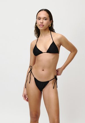 Black bikini featuring a triangular top and tied side bottoms. Smooth texture with thin straps and minimal coverage design. Gold hoop earrings.