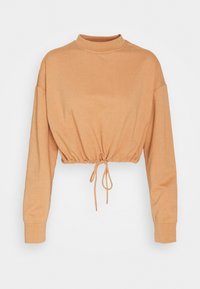 Avskuren långärmad topp i ljusbeige, med hög halsringning och en dragsko i midjan för justerbar passform och form.