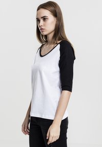 Svart og hvit raglan T-skjorte med trekvart ermer, laget av bomull, rund hals, glatt tekstur, og uten synlige mønstre eller detaljer.