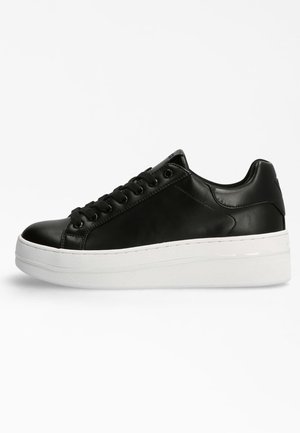 Black leather low-top sneaker with thick white platform sole, black laces, and smooth finish, shown from the side on a white background.