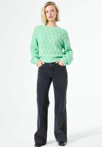 Pull en maille vert menthe avec un motif en losange texturé, associé à un jean noir évasé taille haute, avec une taille ajustée et des jambes larges.