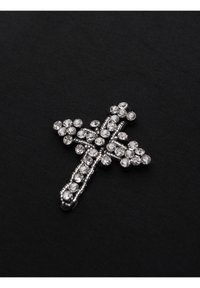 Broche en forme de croix décorée de pierres précieuses rondes et transparentes sur un fond en tissu noir.