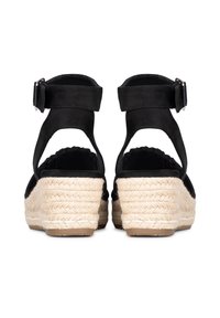 Zoccoli espadrillas in suede nero con cinturino alla caviglia regolabile, tacco avvolto in juta e soletta testurizzata. Presentano un bordo a onde.