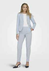 Ljusblå randig blazer och matchande byxor, ihopparat med en vit topp. Tyget är mjukt; byxorna är skräddarsydda med en smal passform.
