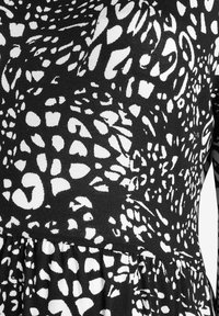 Vestido en blanco y negro con un patrón abstracto de manchas, tejido con una textura y falda fruncida. Diseño de mangas largas.