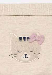 Cremefarbener Stoff mit einem flauschigen, bestickten Katzengesicht; zeigt geschlossene Augen, schwarze Streifen und eine rosa Schleife an einem Ohr.