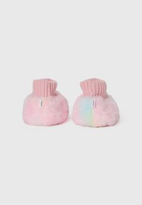 Une paire de chaussons pour bébé en rose doux et duveteux avec des poignets côtelés et de petites étiquettes blanches de la marque sur un fond blanc uni.