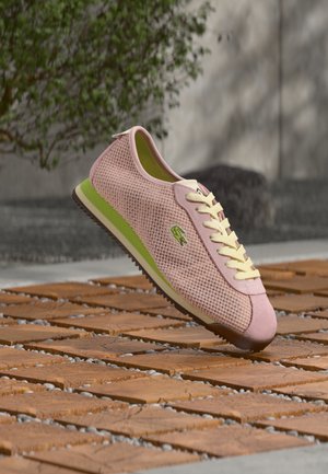 Sneaker Lacoste in mesh rosa con accenti verdi, lacci gialli e suola in gomma, con logo sul lato e dettagli di design testurizzati.