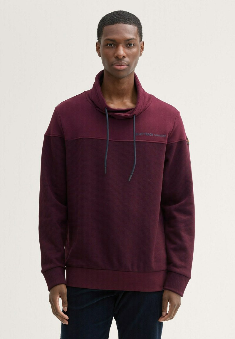 Bordeaux sweatshirt met een kraag, lange mouwen en een gladde textuur. Heeft een contrasterende horizontale naad en koorden.