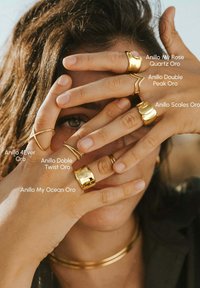 Anelli d'oro di vari design indossati sulle mani, tra cui stili lisci, attorcigliati e testurizzati. È visibile anche una collana d'oro.