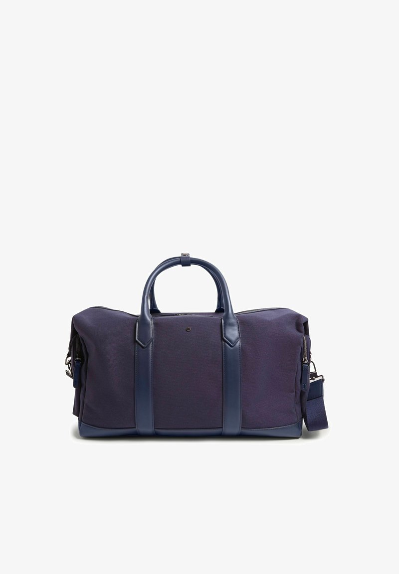 Sac de voyage en tissu bleu foncé avec poignées en cuir, accents en cuir et une bandoulière amovible sur fond blanc.