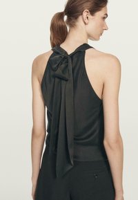 Top in raso nero con design a collo halter, caratterizzato da un grande dettaglio a fiocco e nastri fluttuanti sul retro. Texture liscia, silhouette aderente.