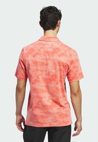 Lyhythihainen korallinvärinen poolopaita, jossa on kuvioitu, abstrakti kuvio. Siinä on klassinen kaulus ja rento istuvuus, sopii vapaa-ajan käyttöön.