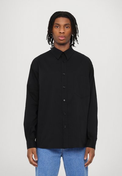 Schwarz langärmliges Hemd mit Knopfverschluss, klassischem Kragen, einer Brusttasche und lässiger Passform, kombiniert mit hellblauen Jeans.