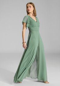 Groene chiffon jumpsuit met een V-hals, fladdermouwtjes en een aansluitende taille. Vloeiende wijde broekspijpen reiken tot de vloer.