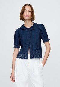 Marinblå blus med korta puffärmar, vågig krage och hålsömsdetaljer vid fållen. Har knäppning framtill och texturerat tyg.