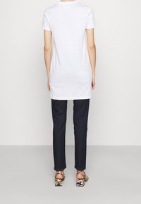 Biała koszulka na krótki rękaw, długi fason, zestawiona z ciemnoniebieskimi dżinsami i sandałami na obcasie w kwiatowy wzór.