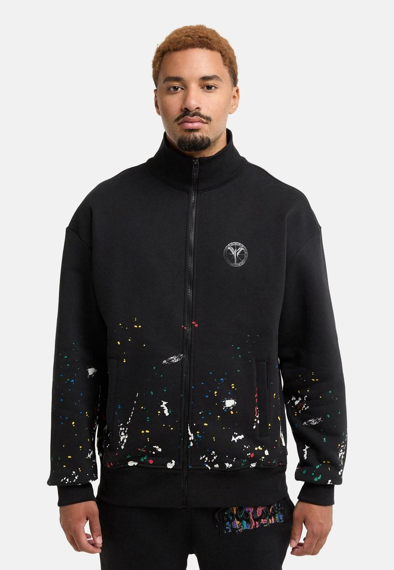 Black zip-up sweatshirt with a high collar; features colorful splatter patterns at the bottom and a logo on the chest. Soft fabric, relaxed fit.