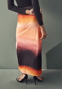 Jupe maxi à motif dégradé avec des nuances de pêche, d'orange et de noir, fabriquée en tissu doux, assortie de sandales à talons noirs.
