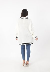 Overdimensioneret hvid striktrøje med høj krave, der har sorte og hvide stribede manchetter og kant. Bæres med blå tætsiddende jeans og gennemsigtige hæle.