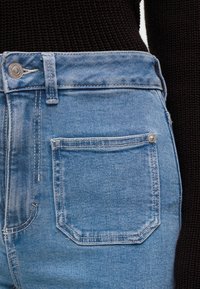 Κοντινό πλάνο της μέσης και της πίσω τσέπης μπλε τζιν με ένα μαύρο πλεκτό πουλόβερ.