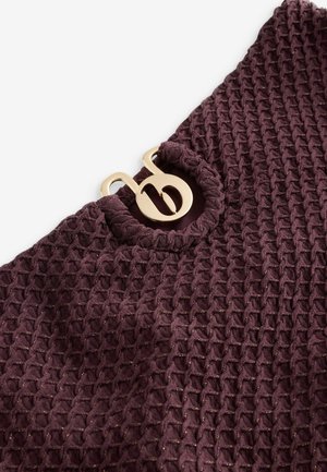 Material texturat de culoare mov închis cu un model tip fagure; prezintă un accent decorativ din metal auriu în zona gâtului.