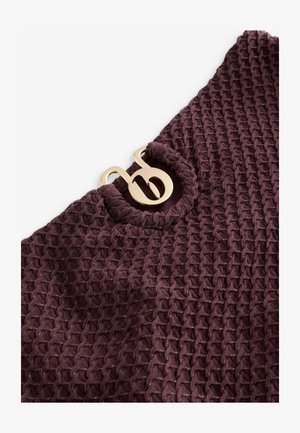 Texturált, sötétlila szövet méhsejtmintával; aranyszínű díszítő fémrészlet található a nyakkivágásnál.