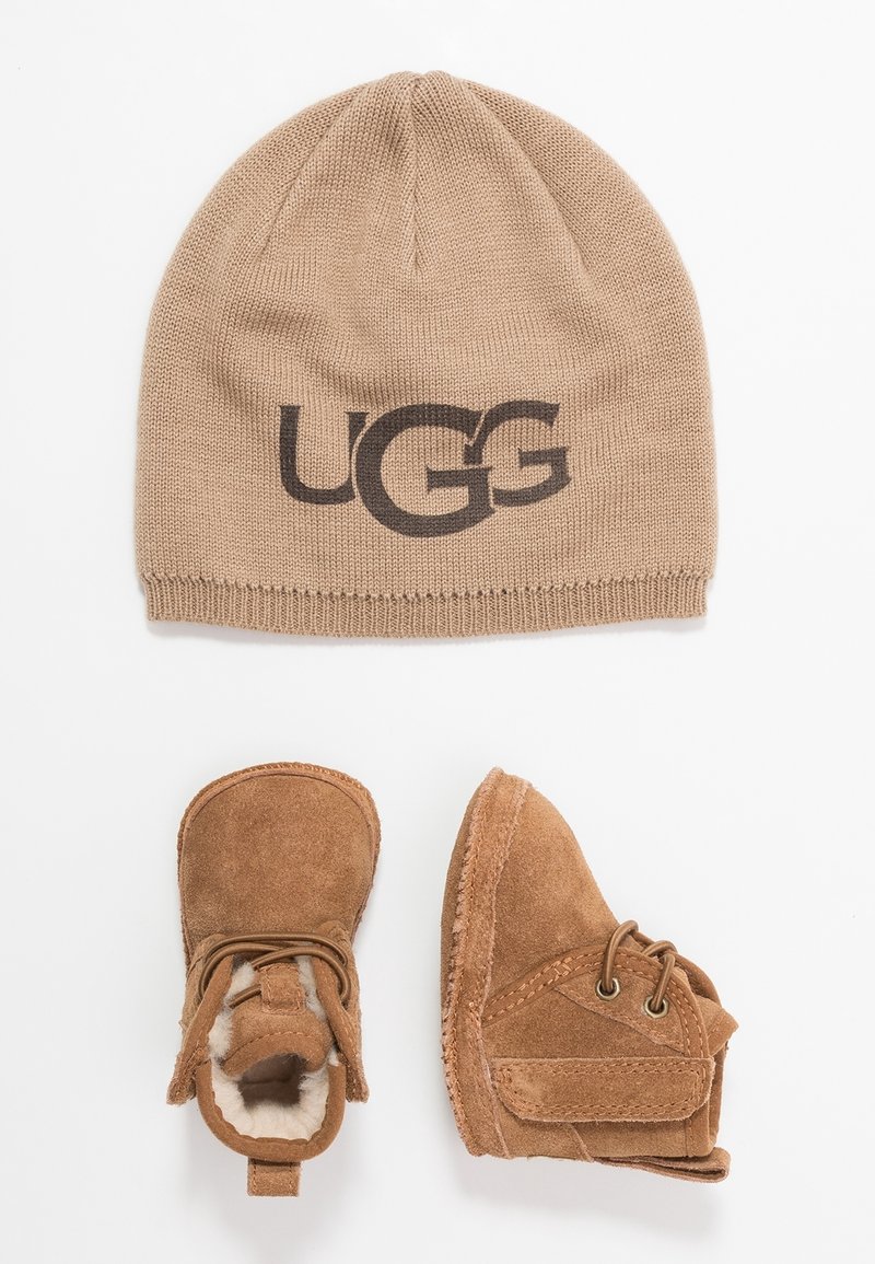 Ruskea neulepipo, jossa on "UGG"-logo, ja ruskeat mokkabootsit vauvoille, joissa on nauhat ja tarranauhakohteet, vuorattu pehmeällä fleecevuorella.