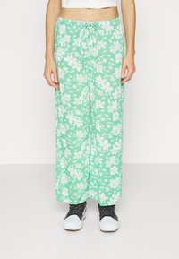 Světlé zelené květinové kalhoty s širokými nohavicemi a bílými vzory květin, vyrobené z lehkého materiálu, s elastickým pasem na stahování a uvolněným střihem.