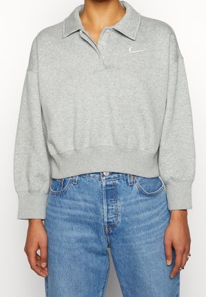 Personne portant un sweat-shirt court gris avec un col et le logo Nike blanc, associé à un jean en denim bleu taille haute.