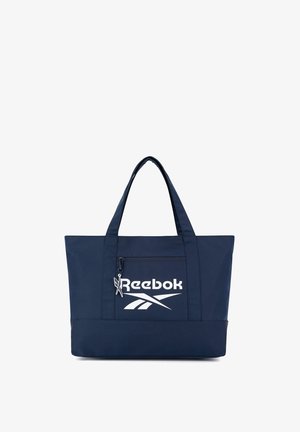 Granatowa torba na ramię Reebok z podwójnymi uchwytami, przednią kieszenią na zamek oraz białym logo Reebok na przednim panelu.