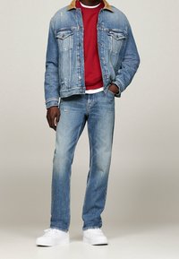 Jeansjacka med beige krage, slitna ljusblå jeans, röd sweatshirt och vita sneakers. Avslappnad passform med dubbla bröstfickor.