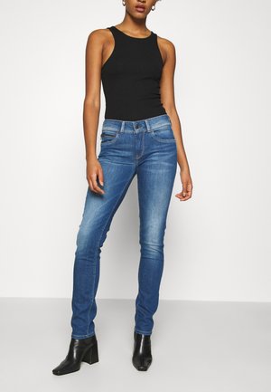 Siniset farkkujen kapeat pillifarkut, joissa keskikorkea vyötärö, viiden taskun malli ja hienovarainen haalistuminen. Yhdistetty istuvaan mustaan hihattomaan toppiin ja mustiin korkokenkiin.