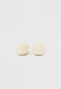 Par de zapatillas crema y peludas con suelas marrones, colocadas lado a lado sobre un fondo blanco liso.